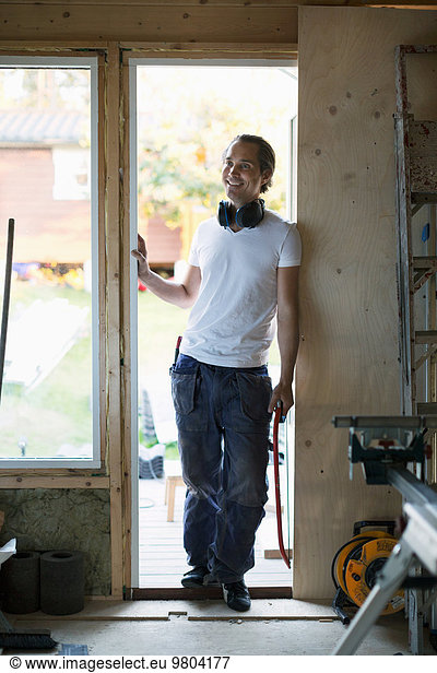 Full length of smiling man leaning in doorway of house being renovated