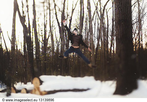 Full length of teenage boy jumping against tree trunks during winter at forest