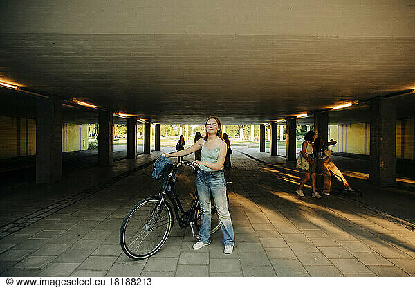 Full length of teenage girl standing with bicycle below bridge