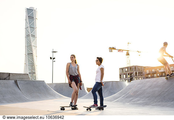 Full length of teenage girls with skateboards at skate park with Turning Torso in background