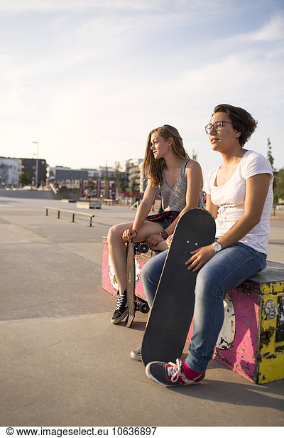 Full length of teenage girls with skateboards sitting on bench at skate park