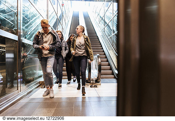 Full length of teenagers walking against escalator