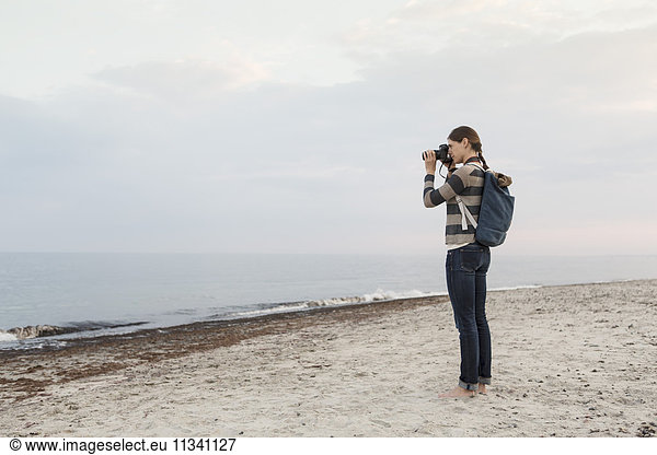 Full length of woman carrying backpack photographing sea against sky