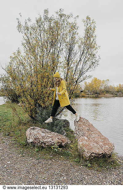 Full length of woman jumping on rocks at lakeshore