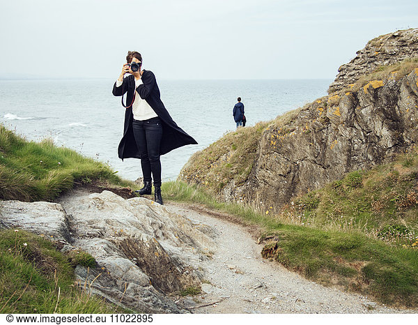 Full length of woman photographing while standing on rock by sea