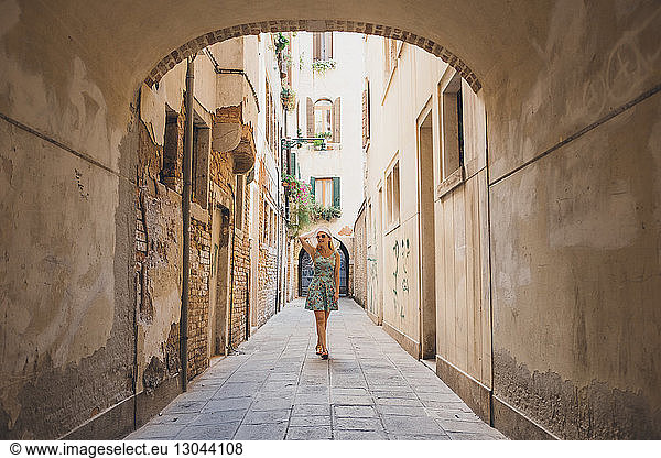 Full length of woman walking in narrow footpath amidst buildings