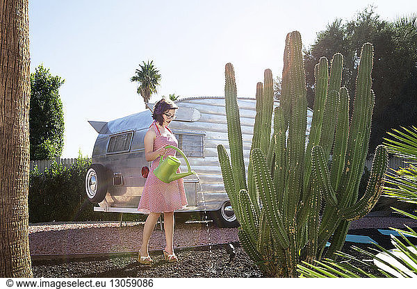 Full length of woman watering cactus while standing against camper van