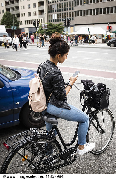 Full length of woman with bicycle using mobile phone while standing at city street