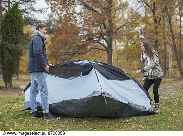 Full length of young couple pitching tent in forest