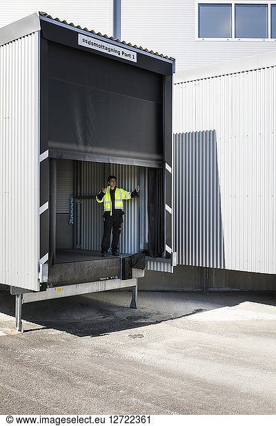 Full length of young male worker gesturing while standing on warehouse entrance