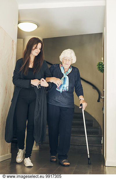 Full length of young woman assisting grandmother to walk by steps