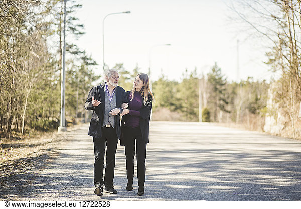 Full length of young woman walking arm in arm with grandfather on road