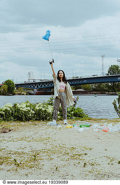 Full length portrait of confident young woman picking garbage near river