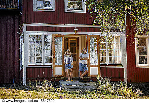 Full length portrait of couple standing at doorway of log cabin