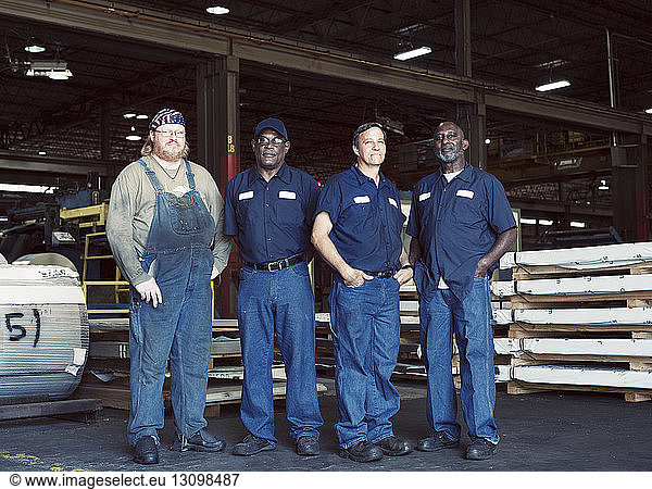 Full length portrait of coworkers standing against manufacturing objects in industry