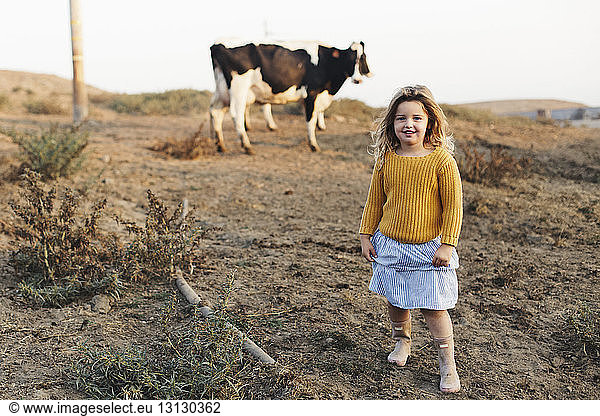 Full length portrait of girl standing on field against cow