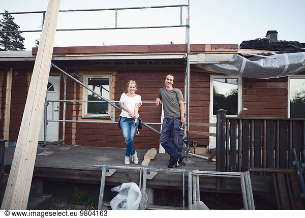 Full length portrait of happy couple leaning on scaffolding of house being renovated