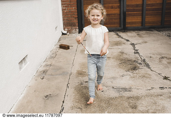Full length portrait of happy girl playing with magic wand outside house