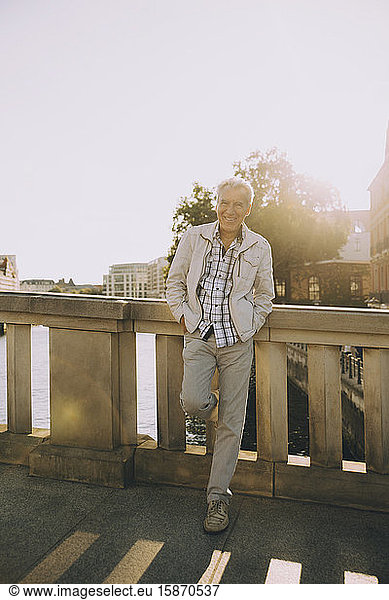 Full length portrait of senior man standing on bridge against railing in city