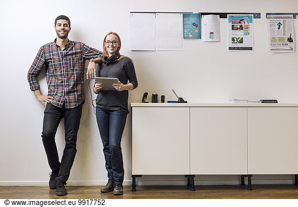 Full length portrait of smiling business colleagues standing by sideboard in creative office