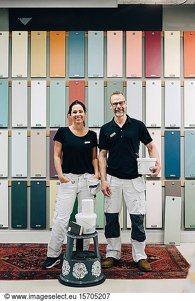 Full length portrait of smiling coworkers standing against multi colored wall in store
