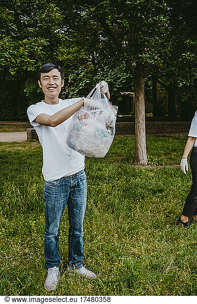 Full length portrait of smiling young male activist holding plastic bag at park