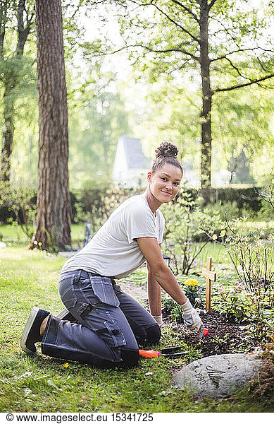 Full length portrait of young woman kneeling while planting at garden