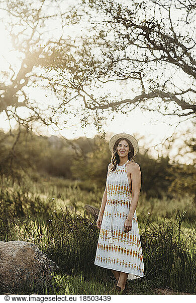 Full length portrait of young woman smiling in backlit meadow