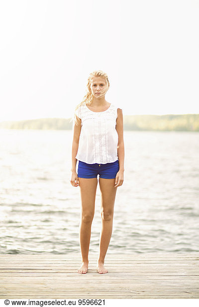 Full length portrait of young woman standing on boardwalk by lake