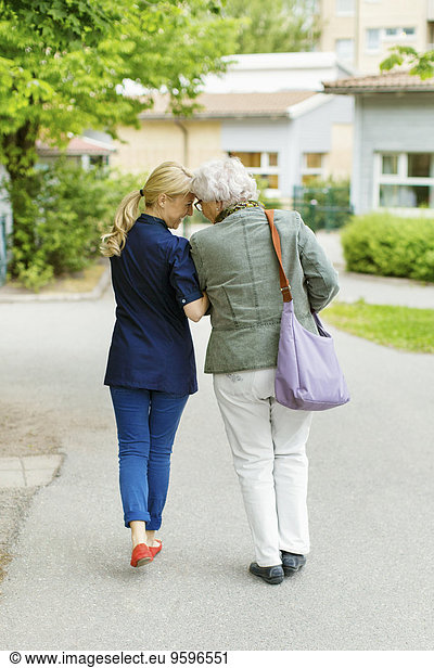 Full length rear view of affectionate female and senior woman walking on street