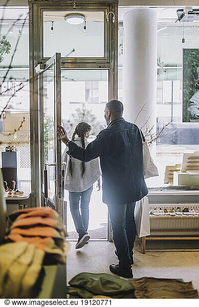 Full length rear view of father and daughter leaving fashion boutique