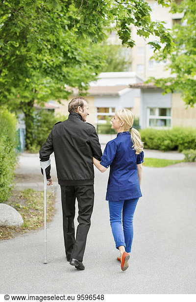 Full length rear view of female walking with disabled senior man on street