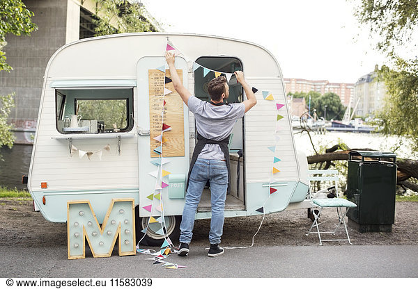 Full length rear view of male owner hanging bunting on food truck