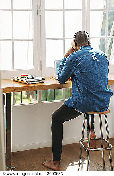 Full length rear view of man working at home office by window