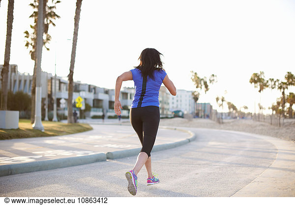 Full length rear view of woman wearing sports clothes jogging in road
