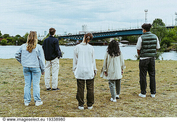 Full length rear view of young friends standing near river