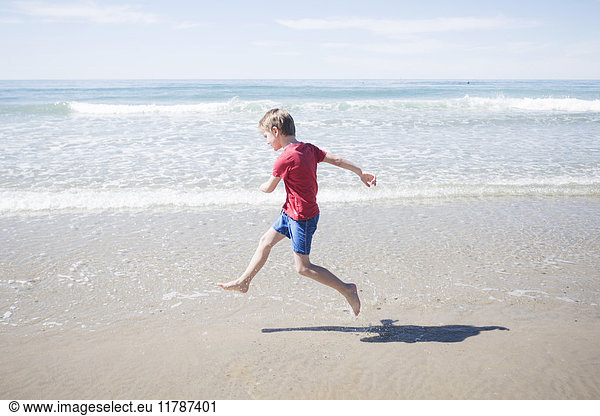 Full length side view of boy running at beach on sunny day