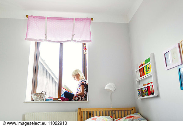Full length side view of girl reading book on window sill