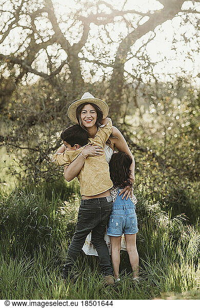 Full length view of mother hugging son and daughter in backlit field
