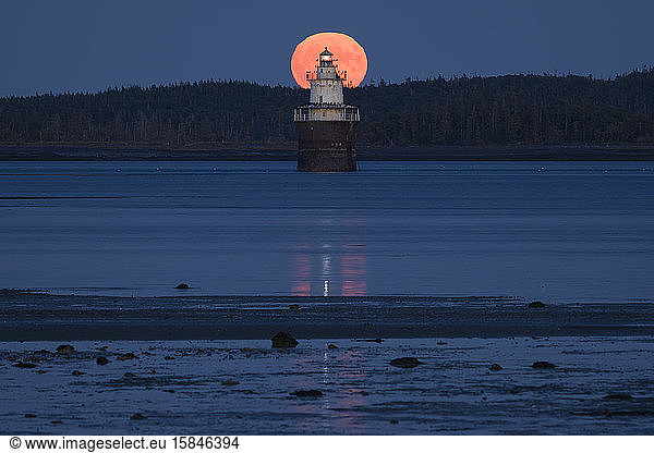 Full moon rising behind a lighthouse and mudflats