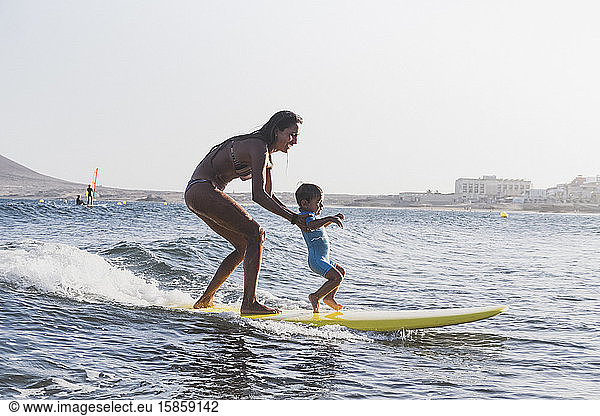 Full view of mother and son surfing a small wave at sea