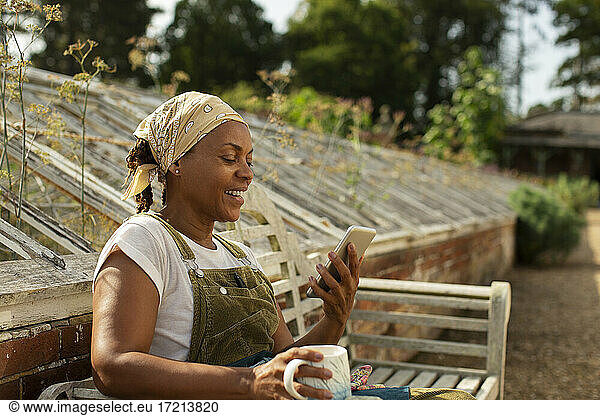 Gärtnereibesitzerin genießt Kaffeepause mit Smartphone