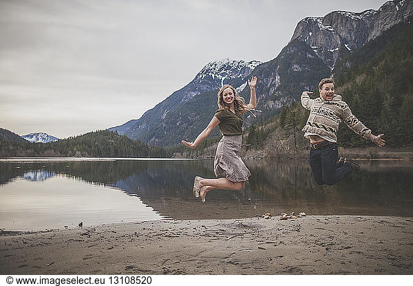 Ganzfiguriges Porträt eines verspielten jungen Paares  das am Seeufer im Silver Lake Provincial Park springt