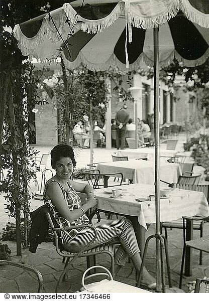 Gardasee im Jahr 1960: junge deutsche Touristin sitzt unter einem Sonnenschirm an einem Tisch eines Restaurants am Hafen von Limone sul Garda  Lombardei  Italien  Europa