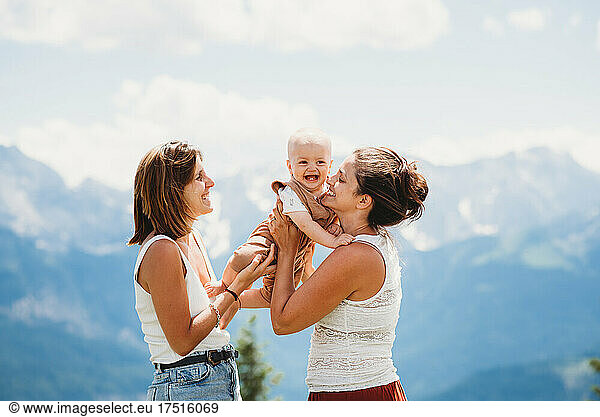 Gay couple holding happy baby in the mountains