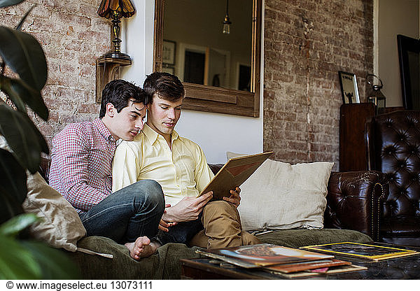 Gay couple holding record cover while sitting on sofa at home