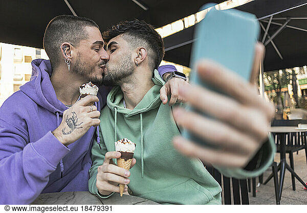 Gay couple kissing and taking selfie over mobile phone at cafe