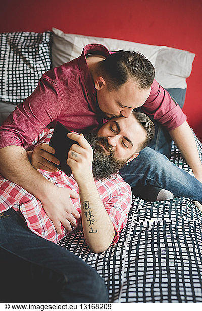 Gay couple kissing and using smartphone in bedroom