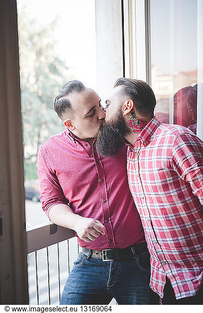 Gay couple kissing by window