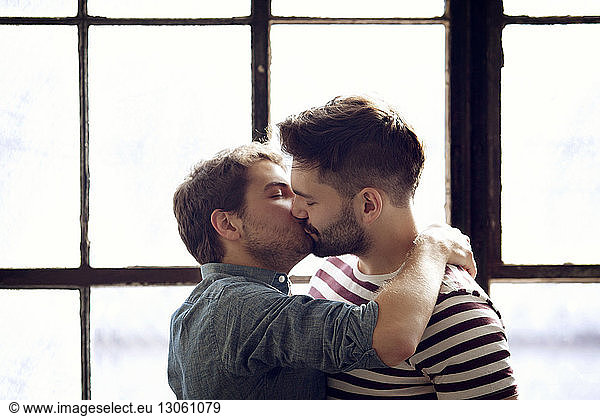 Gay couple kissing by window at home